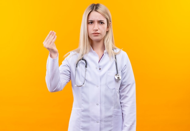 격리 된 노란색 벽에 현금 제스처를 보여주는 의료 가운에 청진기를 착용하는 의사 어린 소녀