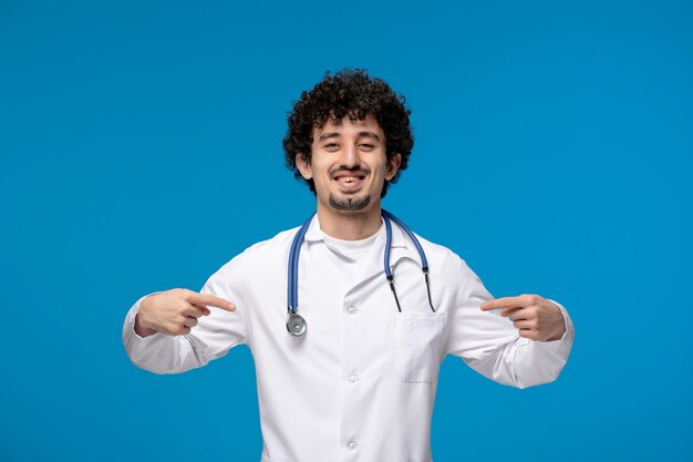 Doctors day curly brunette cute guy in lab coat pointing at himself and smiling