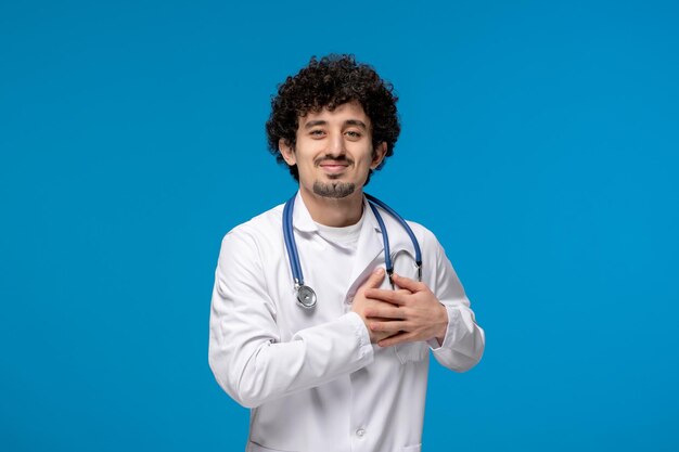 Doctors day curly brunette cute guy in lab coat smiling and holding a chest