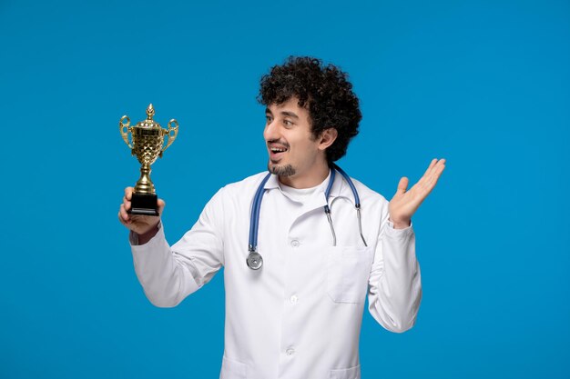 Doctors day curly brunette cute guy in lab coat waving hands and holding a trophy