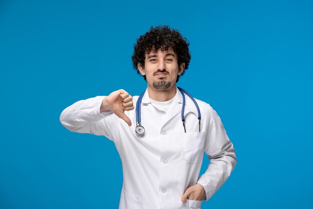 Doctors day curly brunette cute guy in medical uniform showing bad gesture