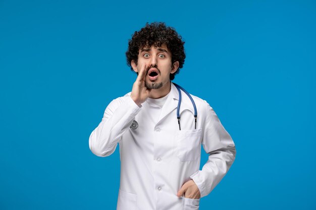 Doctors day curly handsome cute guy in medical uniform calling someone with hands on face