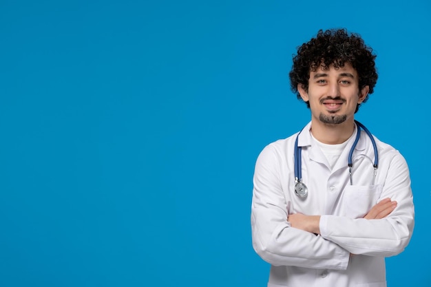 Doctors day curly handsome cute guy in medical uniform crossing hands confidently