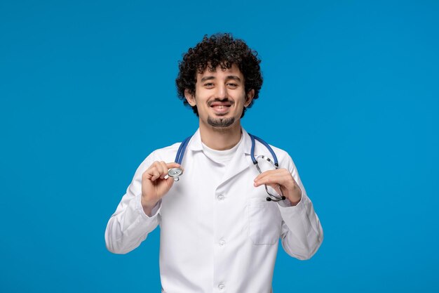 Doctors day curly handsome cute guy in medical uniform holding a stethoscope