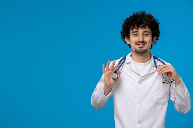 Doctors day curly handsome cute guy in medical uniform holding a stethoscope