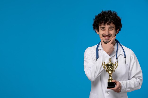 Doctors day curly handsome cute guy in medical uniform smiling and holding a trophy