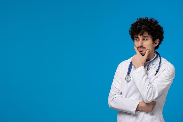 Doctors day curly handsome cute guy in medical uniform thinking and looking far