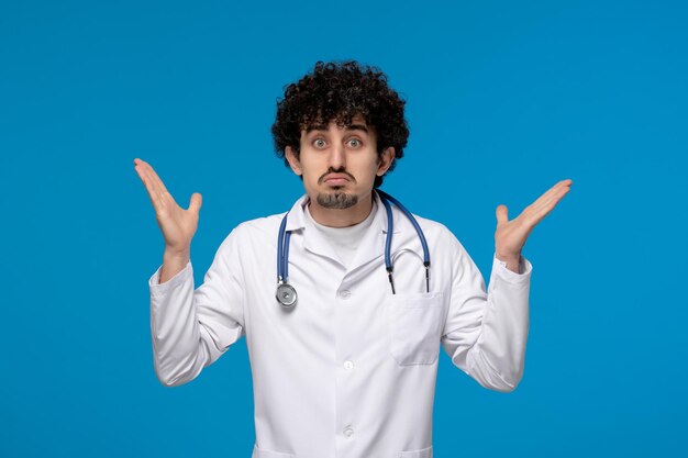 Doctors day curly handsome cute guy in medical uniform waving hands confusingly