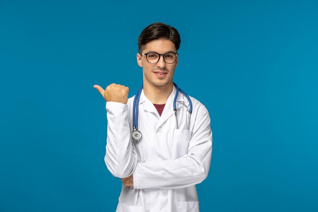 Doctors day cute young brunette guy in lab coat wearing glasses pointing left