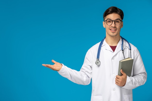Foto gratuita medici giorno carino giovane bell'uomo in camice e occhiali in possesso di un libro