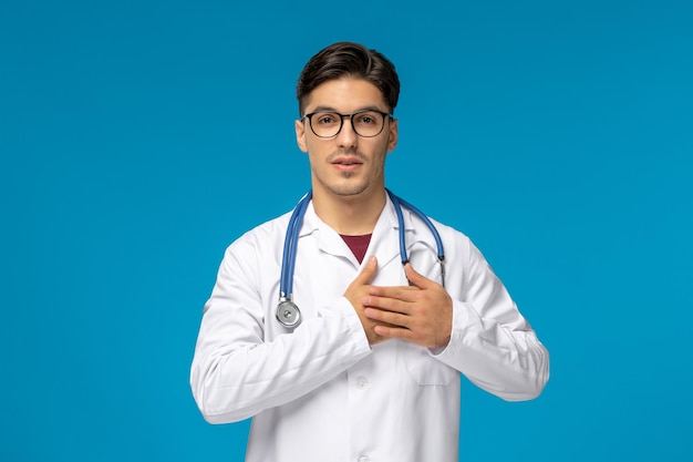Doctors day cute young handsome man in lab coat and glasses holding chest with stethoscope
