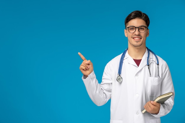 Doctors day cute young handsome man in lab coat and glasses smiling and holding book