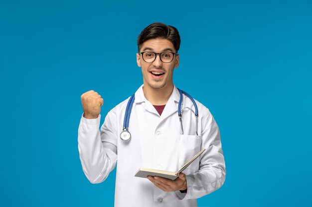 Doctors day handsome brunette cute guy in medical gown excited holding a book