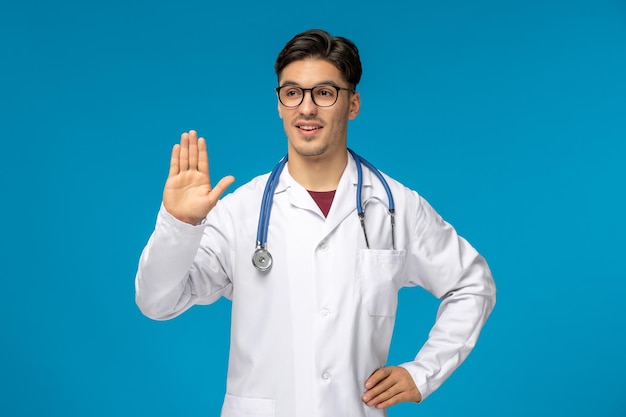 Doctors day handsome brunette cute guy in medical gown showing stop gesture in glasses
