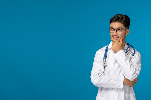 День врача красивый брюнет симпатичный парень в медицинском халате думает и носит очки