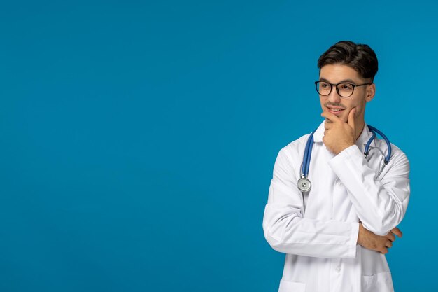 Doctors day handsome brunette cute guy in medical gown thinking and wearing glasses
