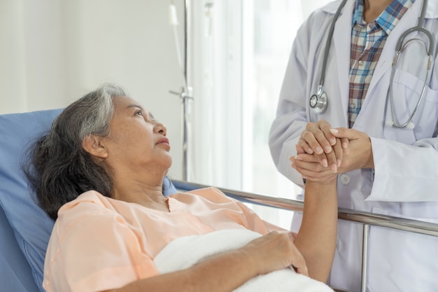 医師は病院-シニア女性の医療とヘルスケアの概念で高齢者のシニア女性患者を奨励するために手を握る