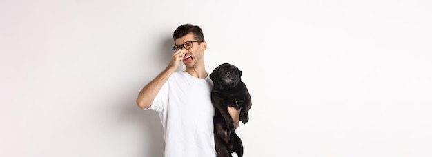 Free photo dog owner squinting and shutting nose from disgusting reek holding pug with bed smell standing over