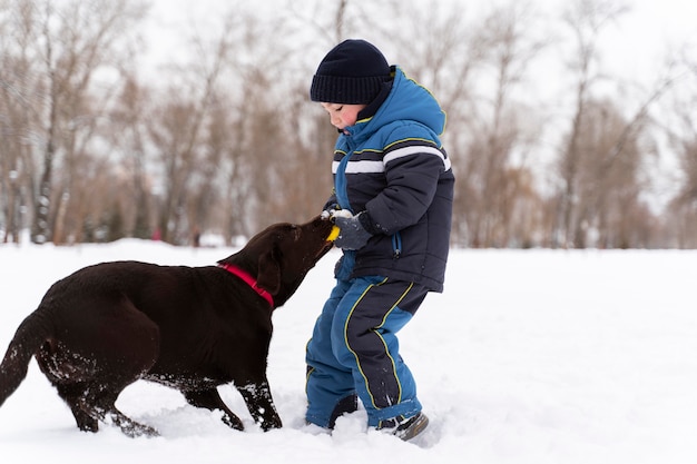 Free photo dog playing with kid in the snow with family