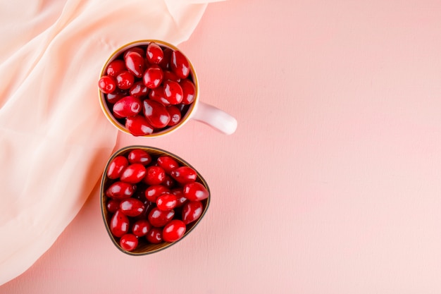 Dogwood berries in cup and bowl on pink and textile.