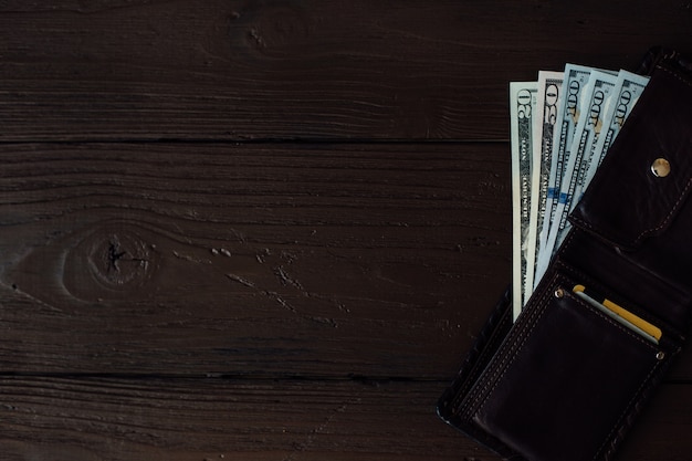 Долларовые банкноты в кожаном мужском кошельке на коричневом деревянном столе
