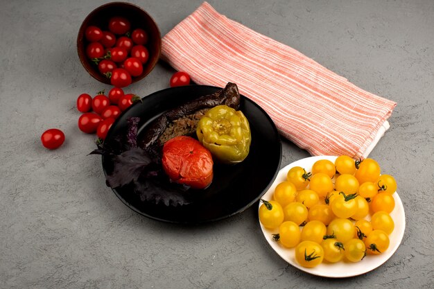 Dolma famous eastern meat dish inside black plate along with red and yellow tomatoes on the bright floor