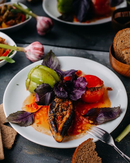 dolma meat meal with purple leafs oil inside white plate along with bread loafs vegetables crisps on grey