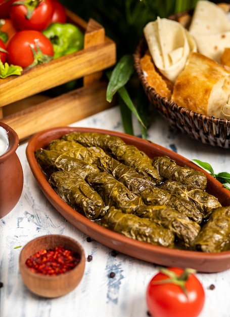 Dolma (tolma, sarma) - stuffed grape leaves with rice and meat. On kitchen table with yogurt, bread, vegetables. Traditional Caucasian, Ottoman, Turkish and Greek cuisine