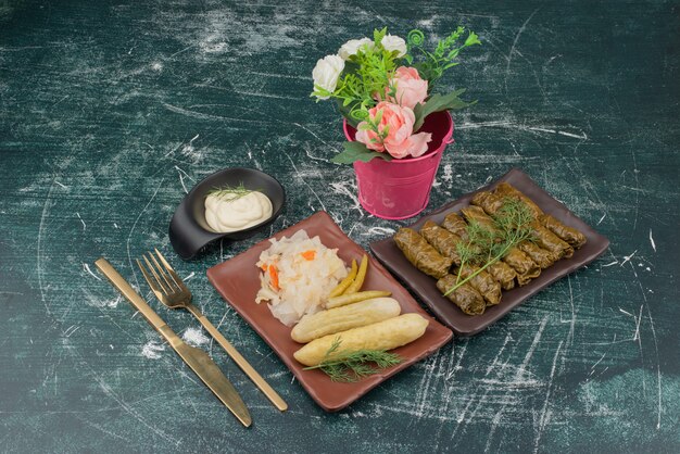 Dolma with sour cream and plate of salt cabbage and cucumber with bucket of lowers .