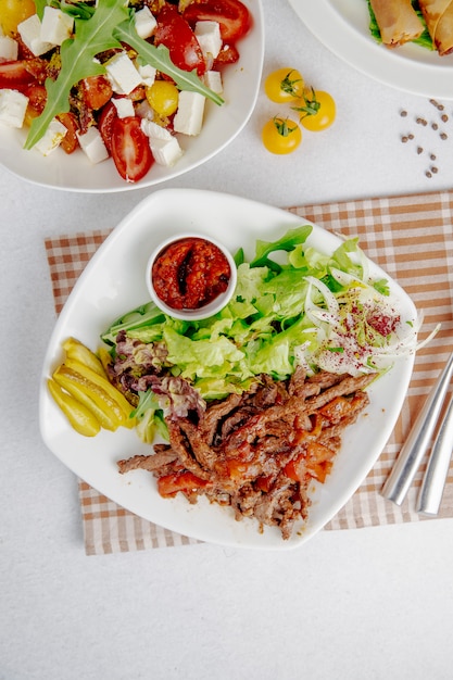 Doner slices with green salad and onions on a white plate