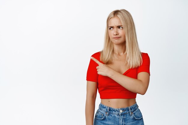 Dont like this Displeased blond woman pointing and looking left showing something upsetting and grimacing from cringe staff white background