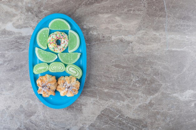 A donut, cookies and marmelades on a small platter on marble surface