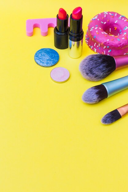 donut; makeup brush; lipstick; and eye shadows on yellow background
