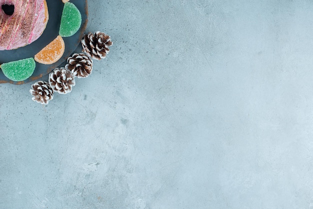 Free photo a donut, marmelades and pine cones on marble.