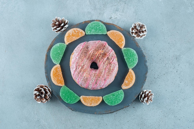 Free photo a donut, marmelades and pine cones on marble.