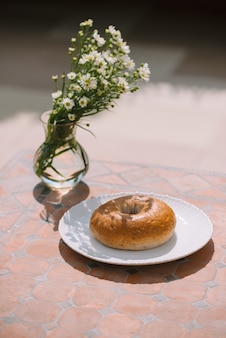 Пончик на белой тарелке на фоне стола при естественном солнечном свете