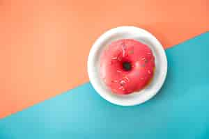 Free photo donut in pink icing on a colored background flat lay