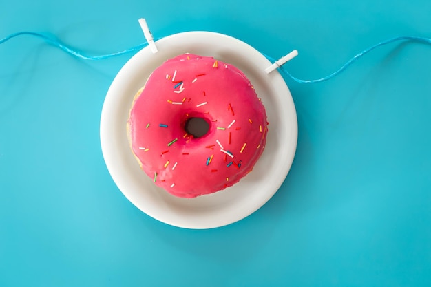Donut in pink icing on a colored background flat lay