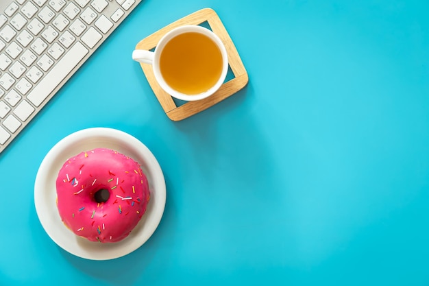 Donut tea and keyboard on a blue background flat lay