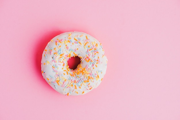 Donut with colorful sprinkles on pink backdrop