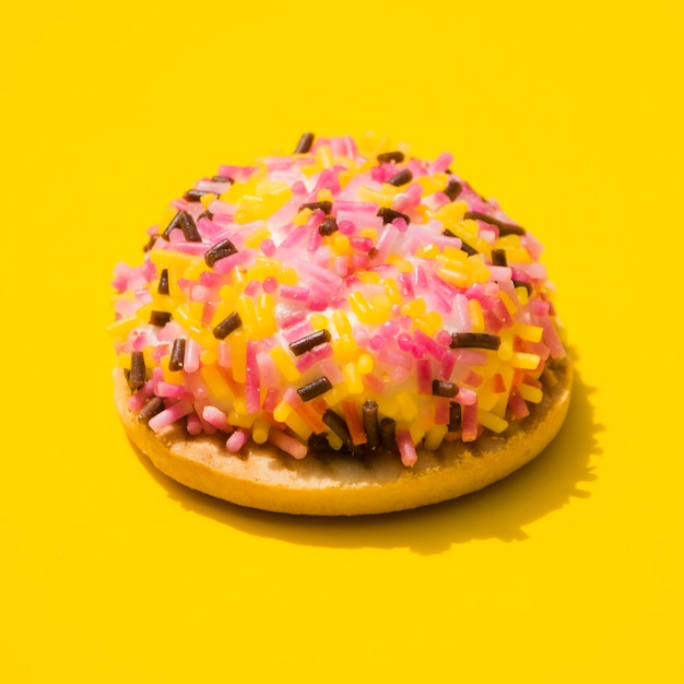 Free photo donut wrapped with sprinkles on yellow background