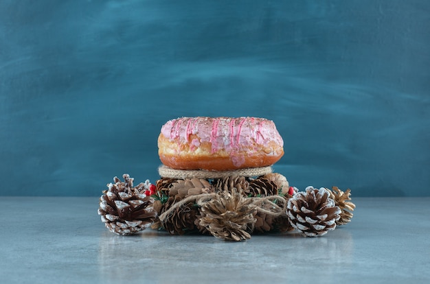 A donut, a wreath and pine cones on marble surface