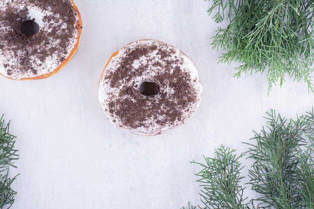 Donuts displayed amid pine leaves on white surface