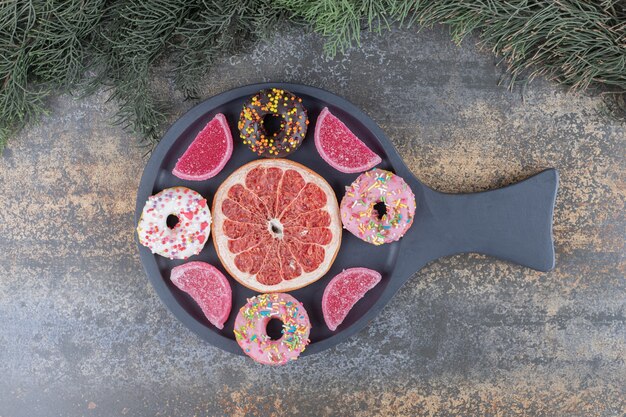 Donuts, marmelades and a grapefruit slice neatly arranged in a serving pan on wooden surface