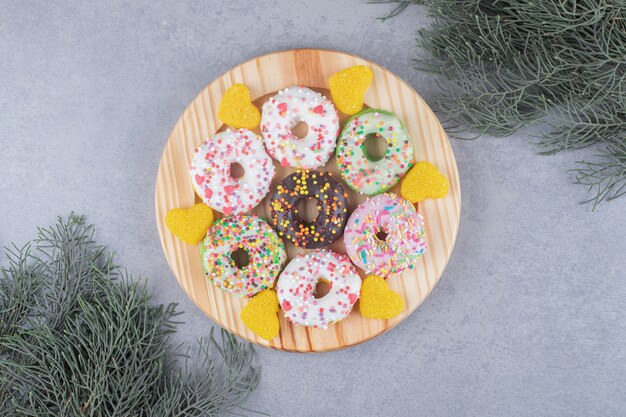 Free photo donuts and marmelades on a platter next to pine branches on marble surface