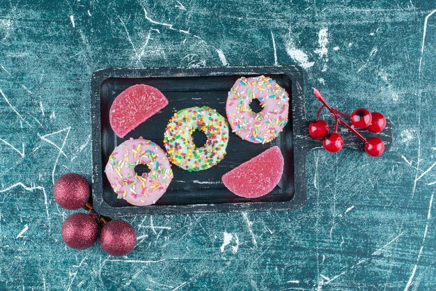 Donuts and marmelades on a small platter next to christmas baubles on blue.