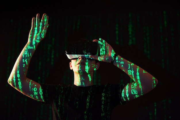 Double exposure of a caucasian man and Virtual reality VR headset is presumably a gamer or a hacker cracking the code into a secure network or server, with lines of code in green