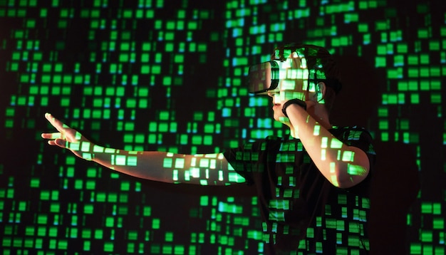 Double exposure of a caucasian man and Virtual reality VR headset is presumably a gamer or a hacker cracking the code into a secure network or server, with lines of code in green