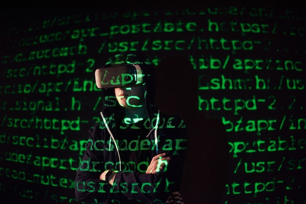 Double exposure of a caucasian man and Virtual reality VR headset is presumably a gamer or a hacker cracking the code into a secure network or server, with lines of code in green