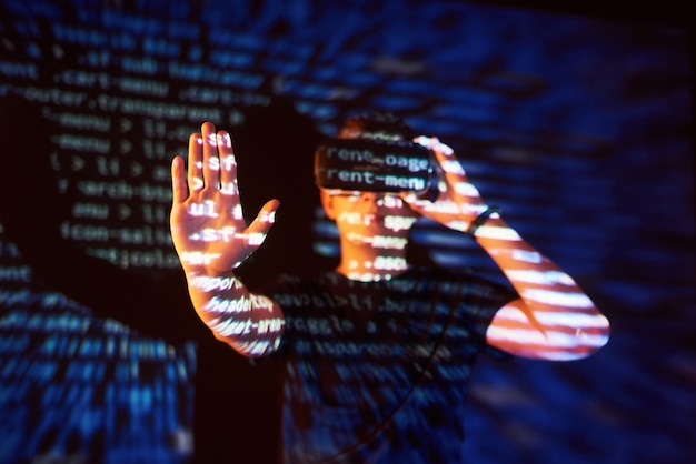 La doppia esposizione di un uomo caucasico e un visore vr per realtà virtuale è presumibilmente un giocatore o un hacker che cracka il codice in una rete o un server sicuro, con linee di codice